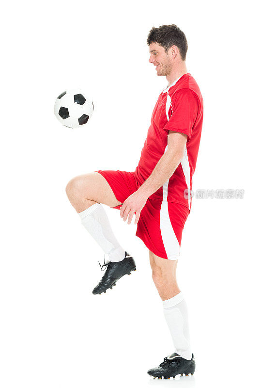 全身/一人/一人/侧视/ 30-39岁英俊的人的侧面视图高加索男性/中年成年男子/中年成人足球运动员杂耍/踢在白色背景下穿着足球制服/运动/膝盖